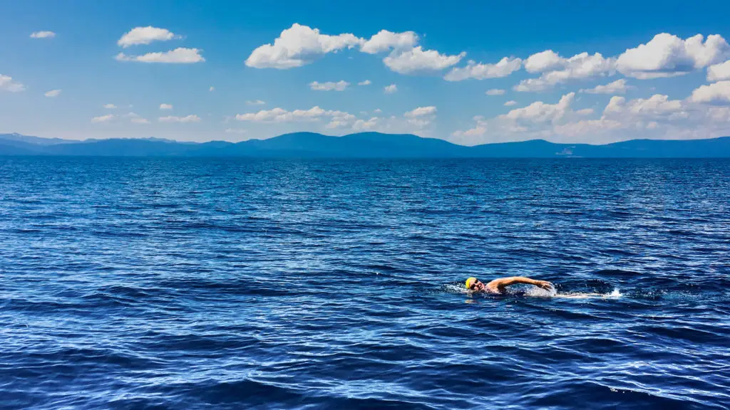 Swimmer wearing a yellow cap completing a solo open water swim across Lake Tahoe under a blue sky with mountain ranges in the distance.