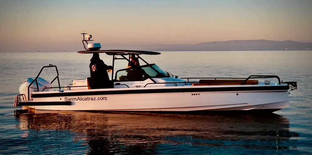 A modern Axopar 28 escort vessel from SwimAlcatraz.com floats in calm water at sunrise, equipped for open water swimming support.