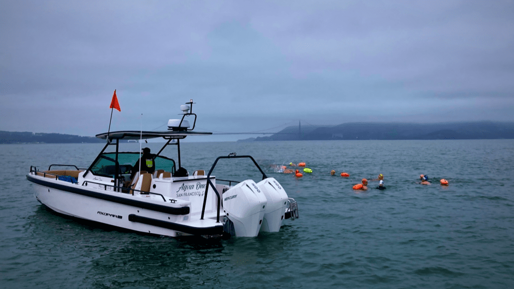 Swimmers in San Francisco Bay near an Axopar escort vessel with the Golden Gate Bridge in the background.